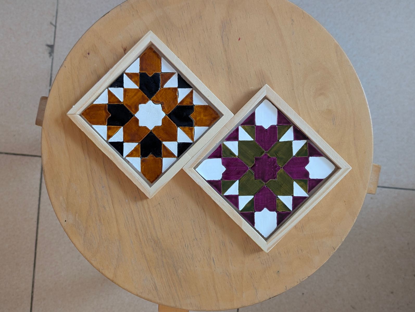 Dos posavasos de mosaico geométrico terminados sobre un taburete de madera